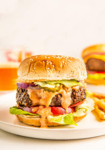 A hamburger dressed with In and Out sauce on a white plate.