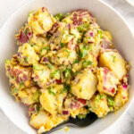 Bowl of red potato salad with celery, onions, and creamy mayo dressing.