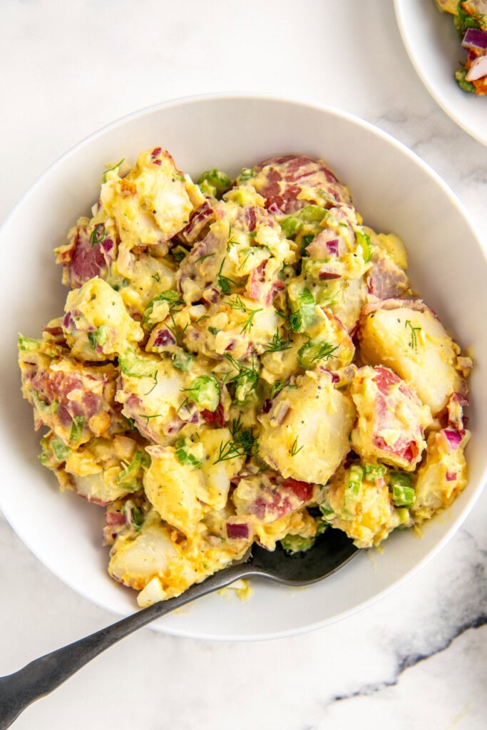 Bowl of red potato salad with celery, onions, and creamy mayo dressing.