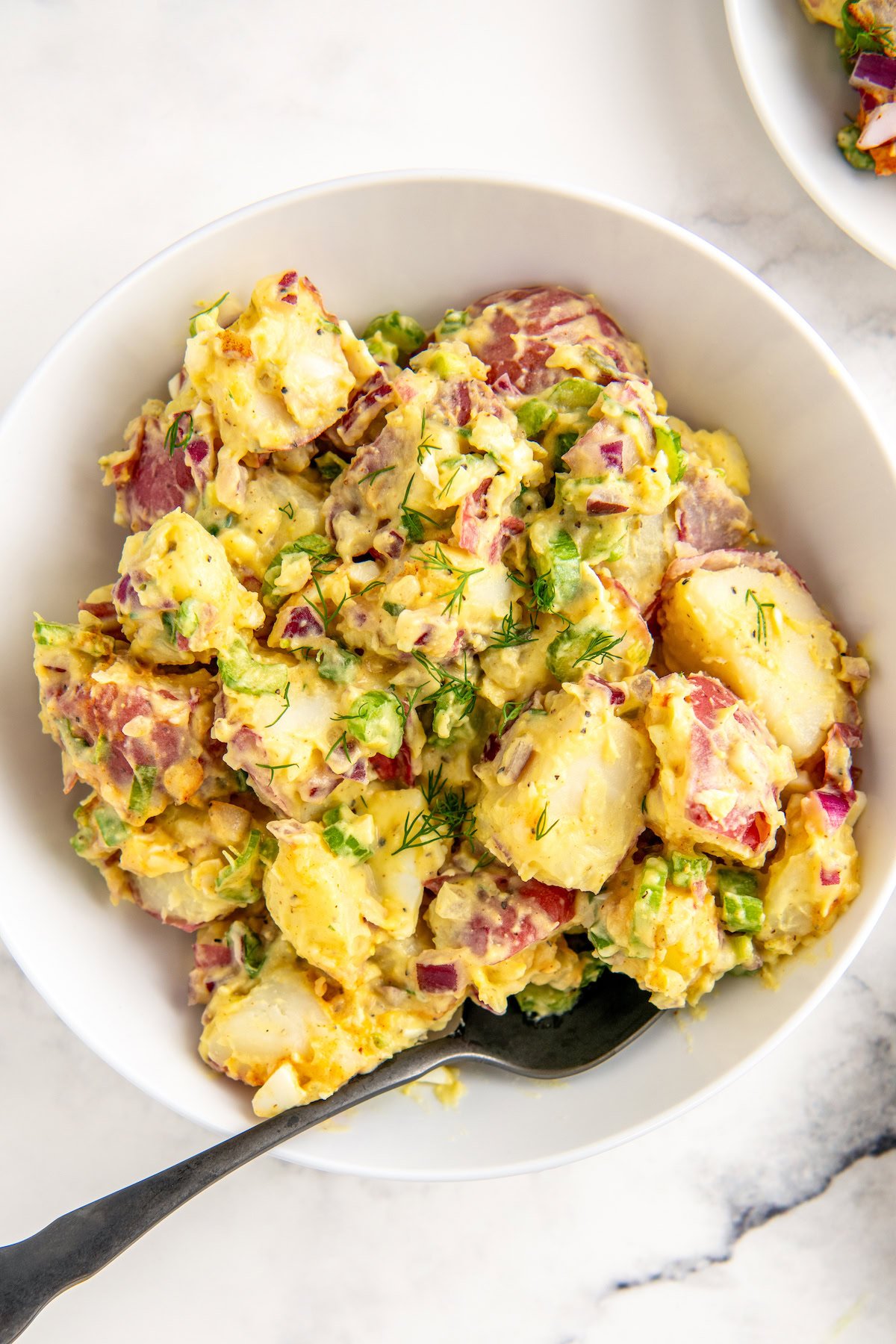 A large serving bowl of creamy red potato salad with egg, celery, onions, and creamy mayo-dill dressing. 