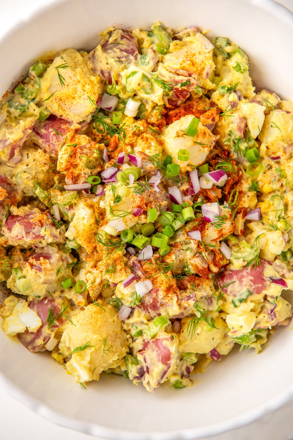 Overhead view of the creamy southern potato salad recipe with egg served in a bowl topped with smoked paprika, green onion and fresh dill.