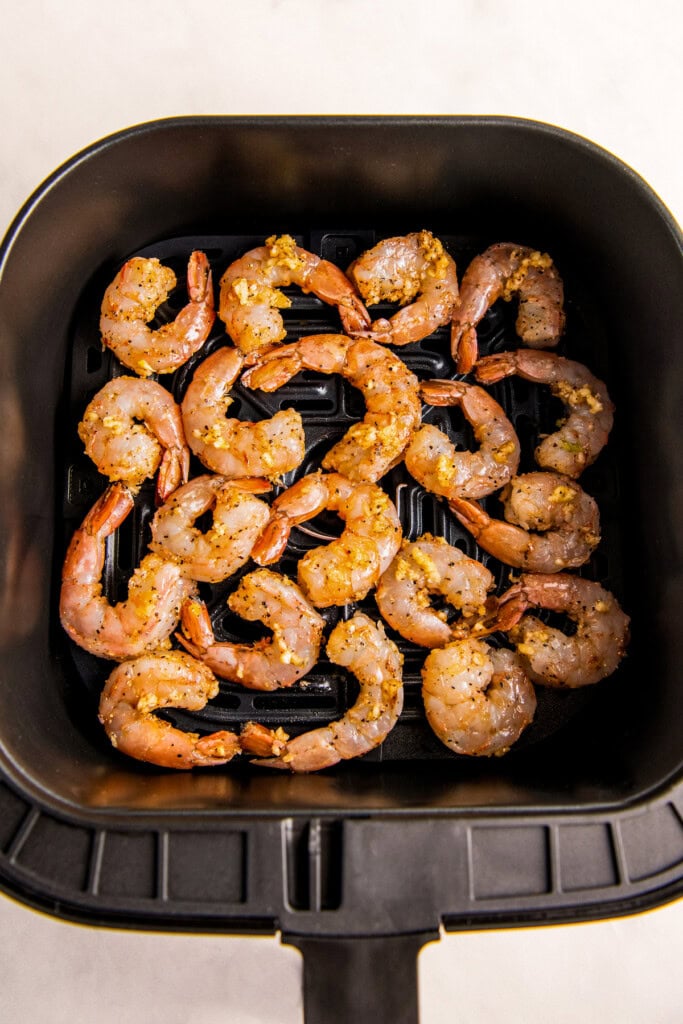 Uncooked shrimp in air fryer basket arranged in an even layer.