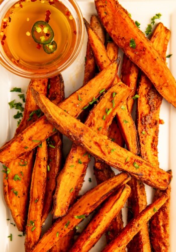 A bunch of garlicky air fryer sweet potato wedges with hot honey on the side.