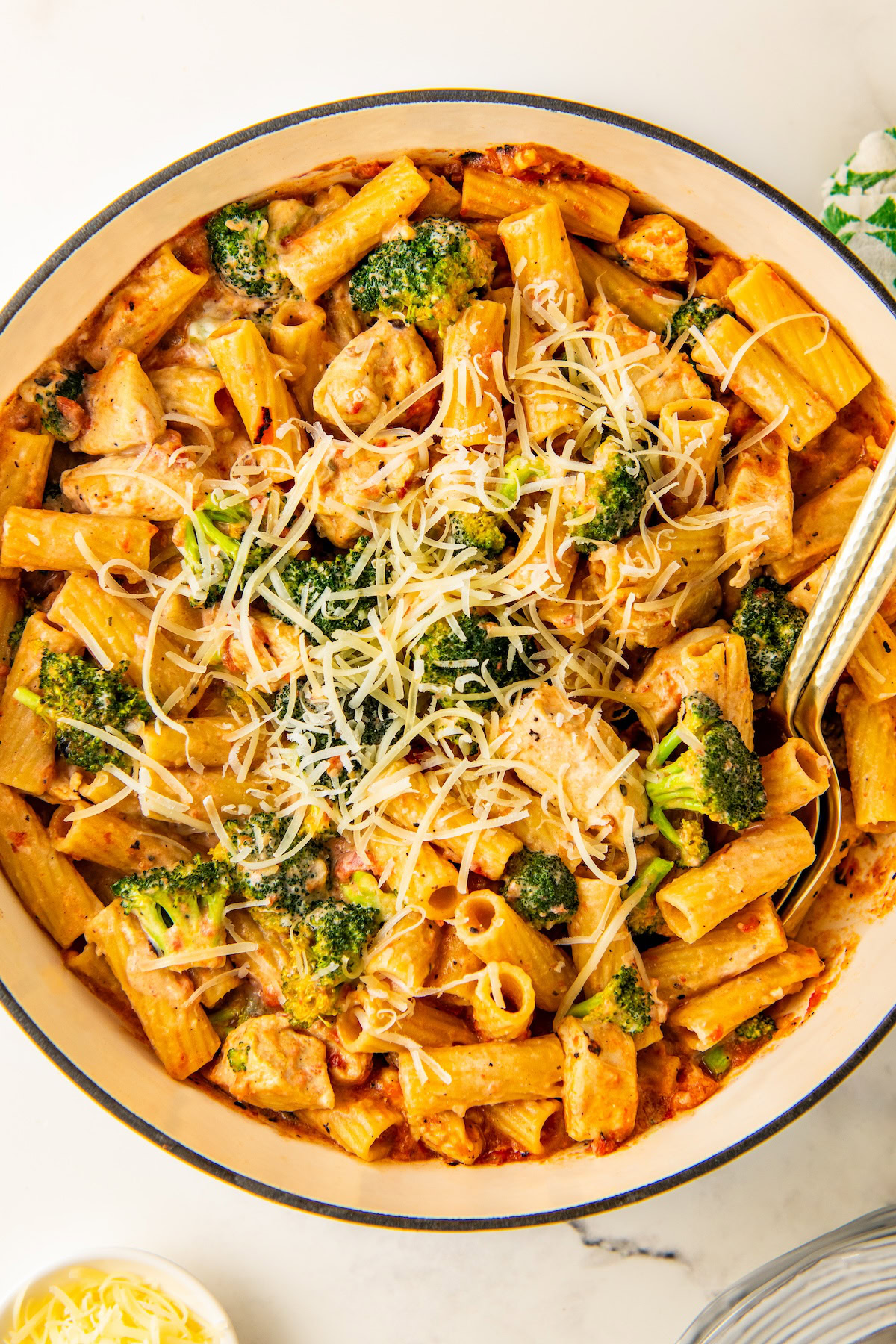 A pot of creamy boursin cheese pasta with chicken and broccoli topped with shredded parmesan cheese with two serving spoons on the side.