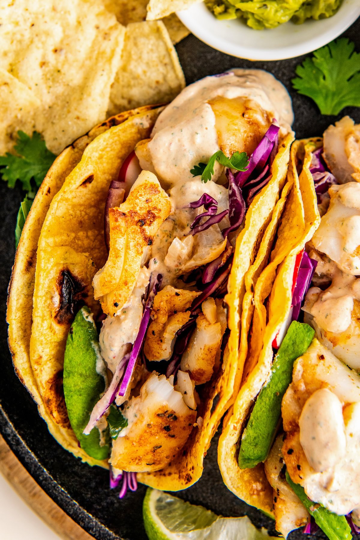 Two easy fish tacos with flaky, seasoned white fish and warm corn tortillas arranged on a plate with all the toppings piled on top.