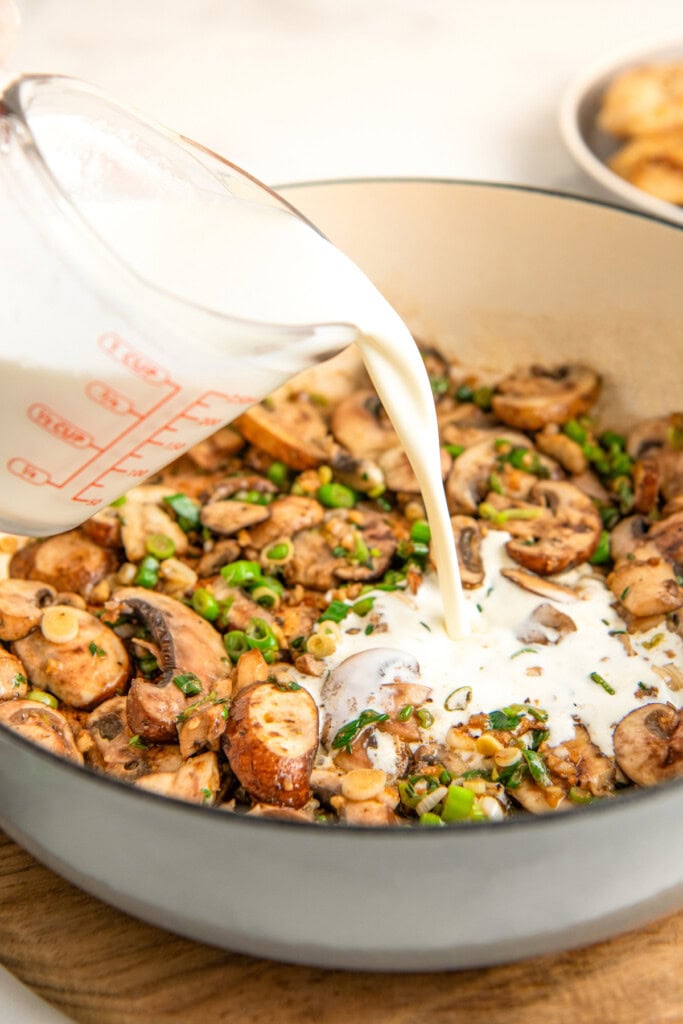 Pouring the heavy cream into the skillet filled with sautéed mushrooms, garlic, green onions and thyme. 