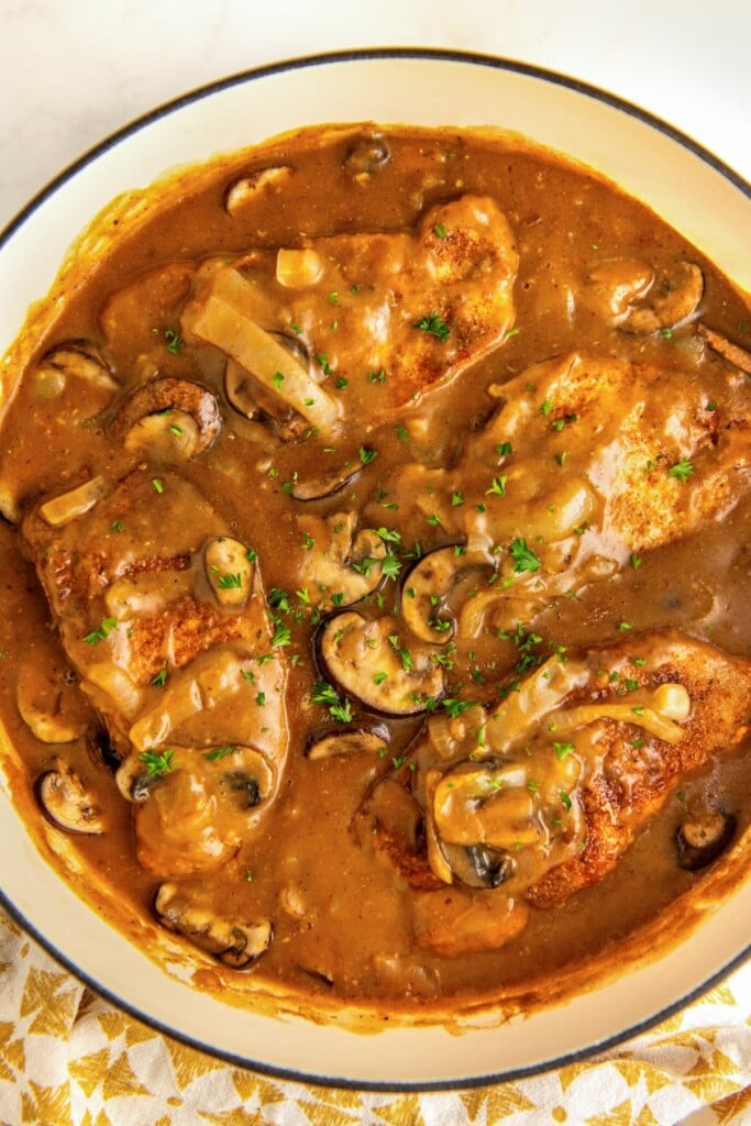 Seared pork chops smothered in a rich brown mushroom gravy in a large skillet.
