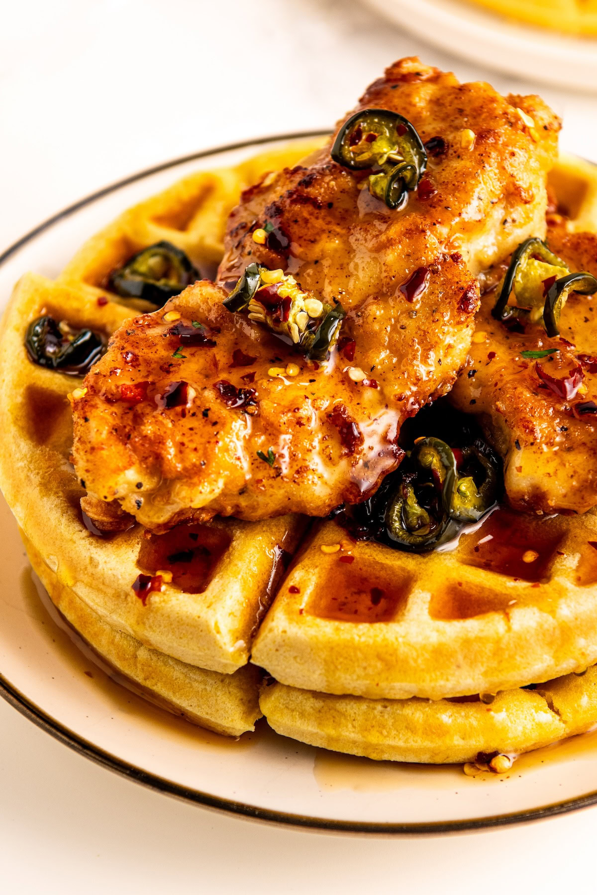 Southern style chicken and waffles on a plate with juicy fried chicken, two cornbread waffles and a hearty drizzle of hot honey.