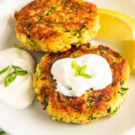 Two crispy, golden brown zucchini fritters on a plate topped with sour cream.