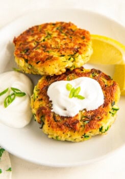 Two crispy, golden brown zucchini fritters on a plate topped with sour cream.