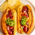 Two hot dogs stuffed with jalapeño popper filling and topped with melty cheddar cheese and crispy bacon.