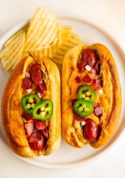 Two hot dogs stuffed with jalapeño popper filling and topped with melty cheddar cheese and crispy bacon.