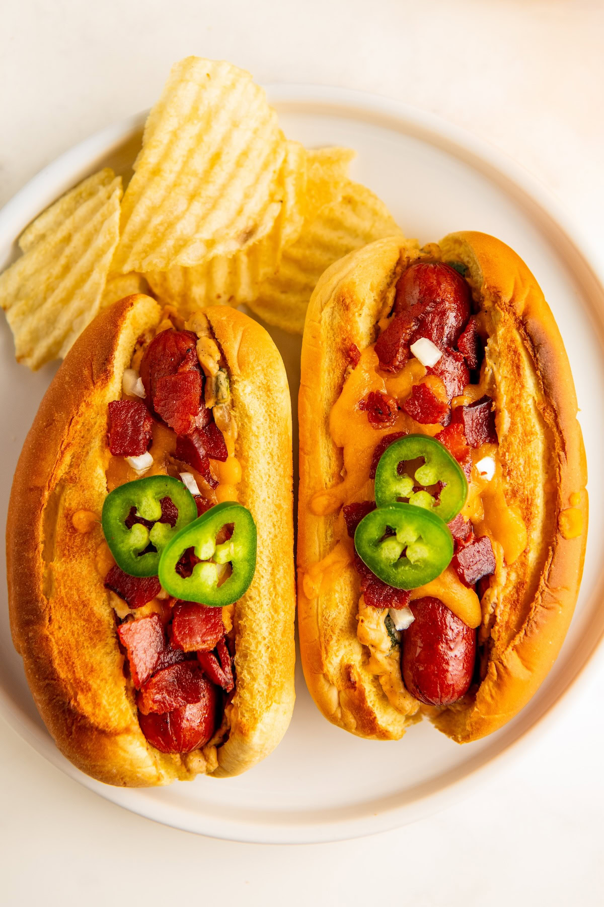 Two hot dogs stuffed with jalapeño popper filling and topped with melty cheddar cheese and crispy bacon.