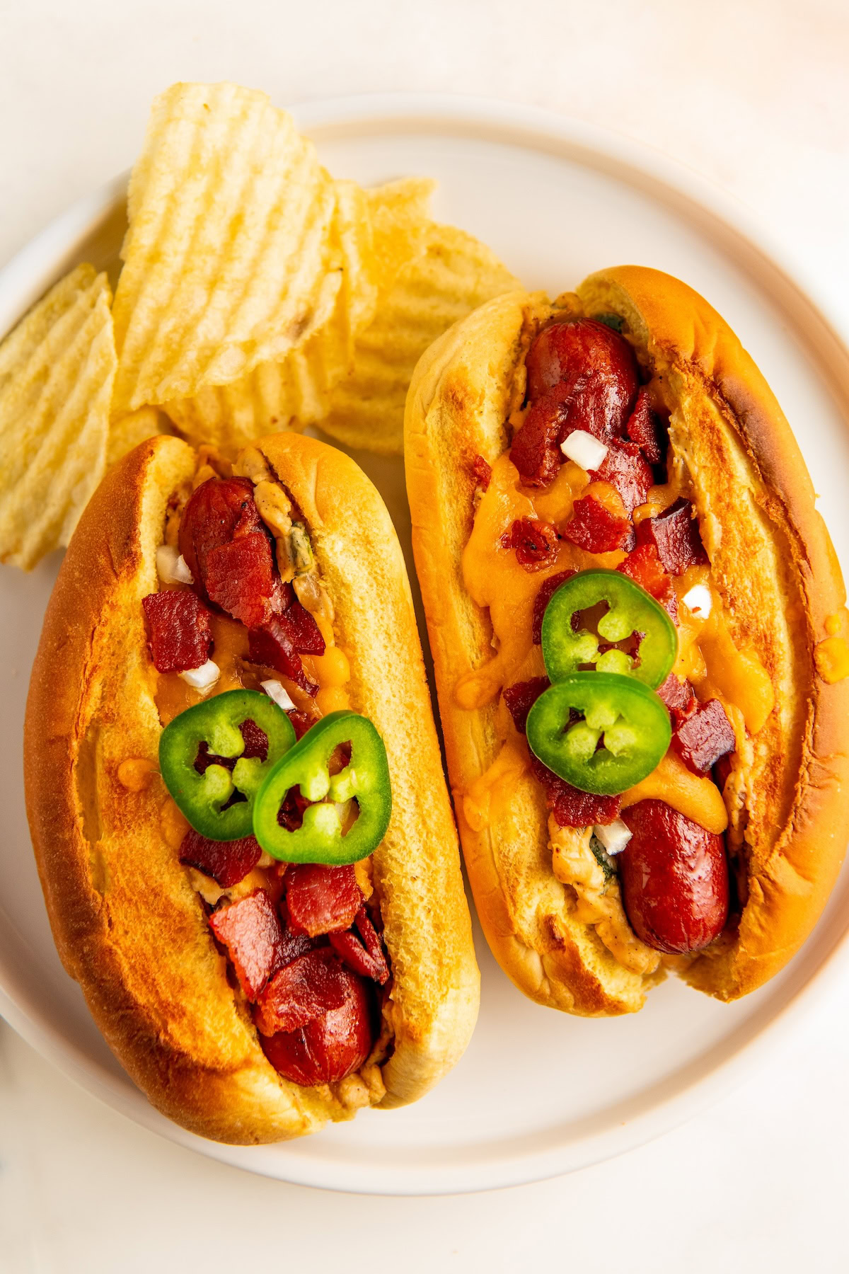 Two jalapeño popper hot dogs with potato chips on the side. 