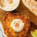 A bowl of creamy tajin sauce with the sauce added on top of a stack of zucchini fritters and slathered on grilled corn with a sprinkle of more tajin on top.