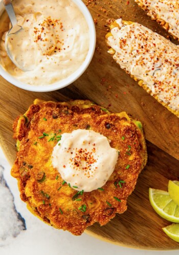 A bowl of creamy tajin sauce with the sauce added on top of a stack of zucchini fritters and slathered on grilled corn with a sprinkle of more tajin on top.