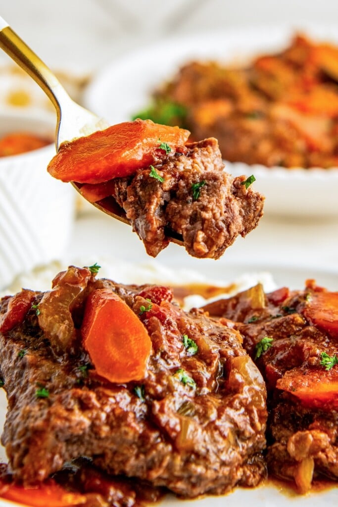 A fork cutting a bite of crockpot Swiss steak.