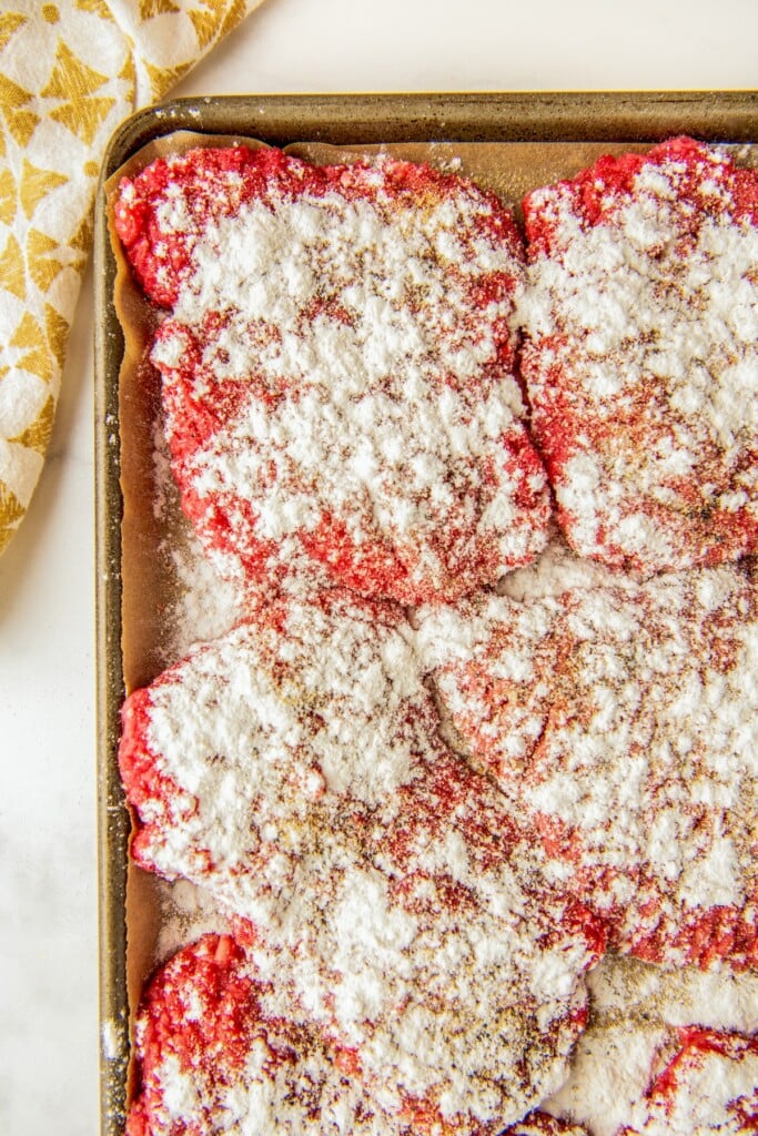 Swiss steak coated in seasonings and flour on a baking sheet lined with parchment paper.