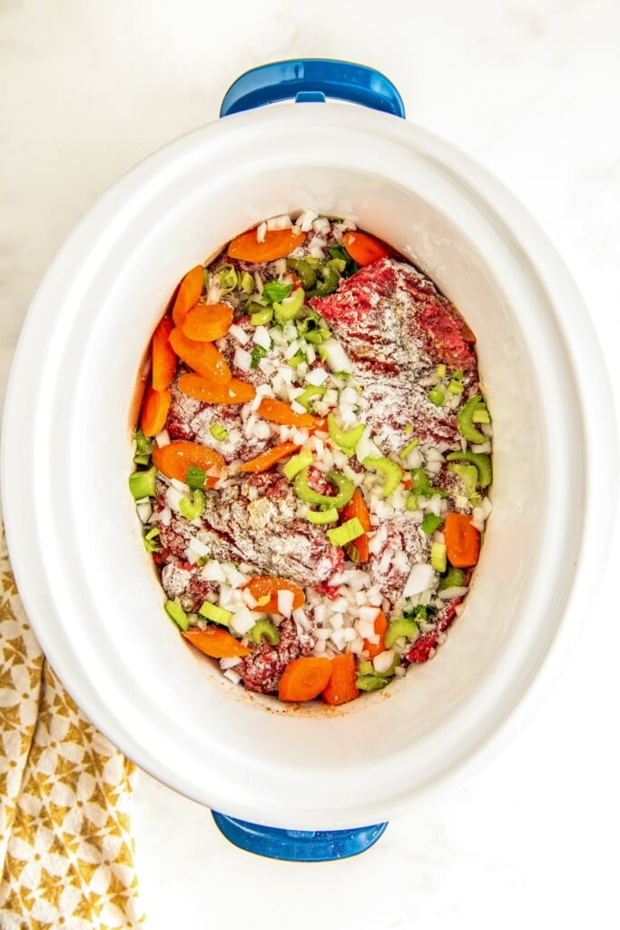 Seasoned and floured steak in crockpot with chopped vegetables.