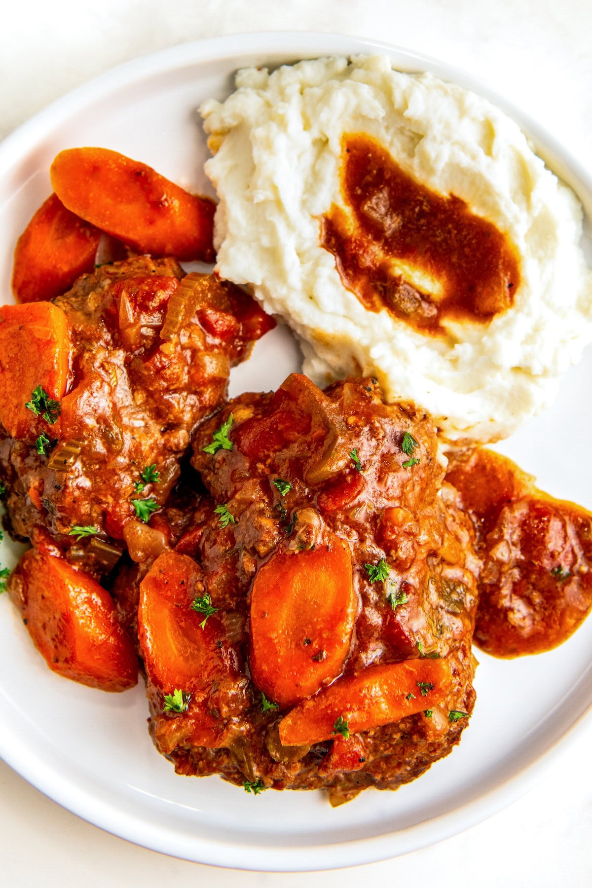 Juicy and tender slow cooker Swiss steak with gravy and carrots served on the side of mashed potatoes.