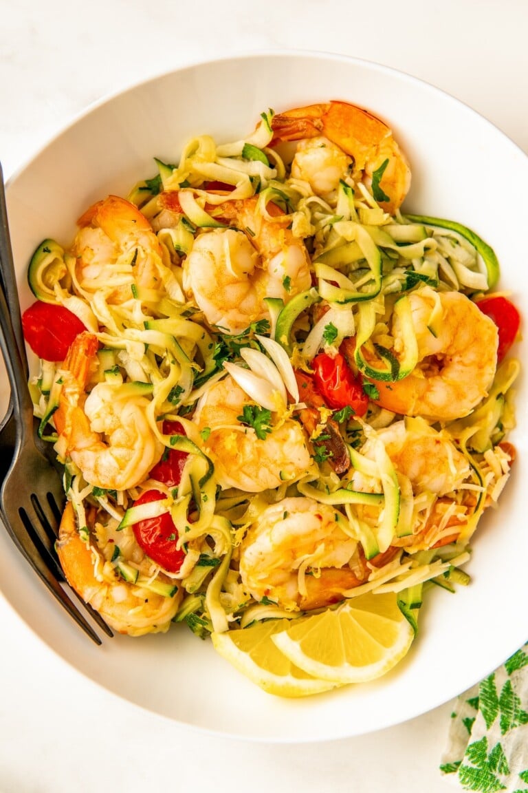 Bowl of lemon garlic shrimp zoodles with parmesan, parsley, and juicy tomatoes.