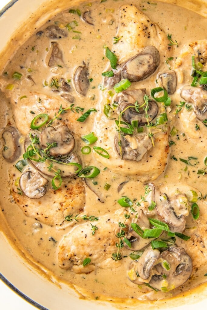 Creamy asiago chicken and mushrooms in a skillet topped with fresh herbs.