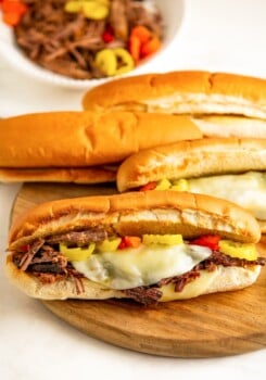 Several beef sandwiches on freshly-toasted bread, with melty cheese and pickled veggies.