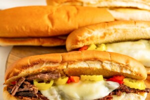Several beef sandwiches on freshly-toasted bread, with melty cheese and pickled veggies.
