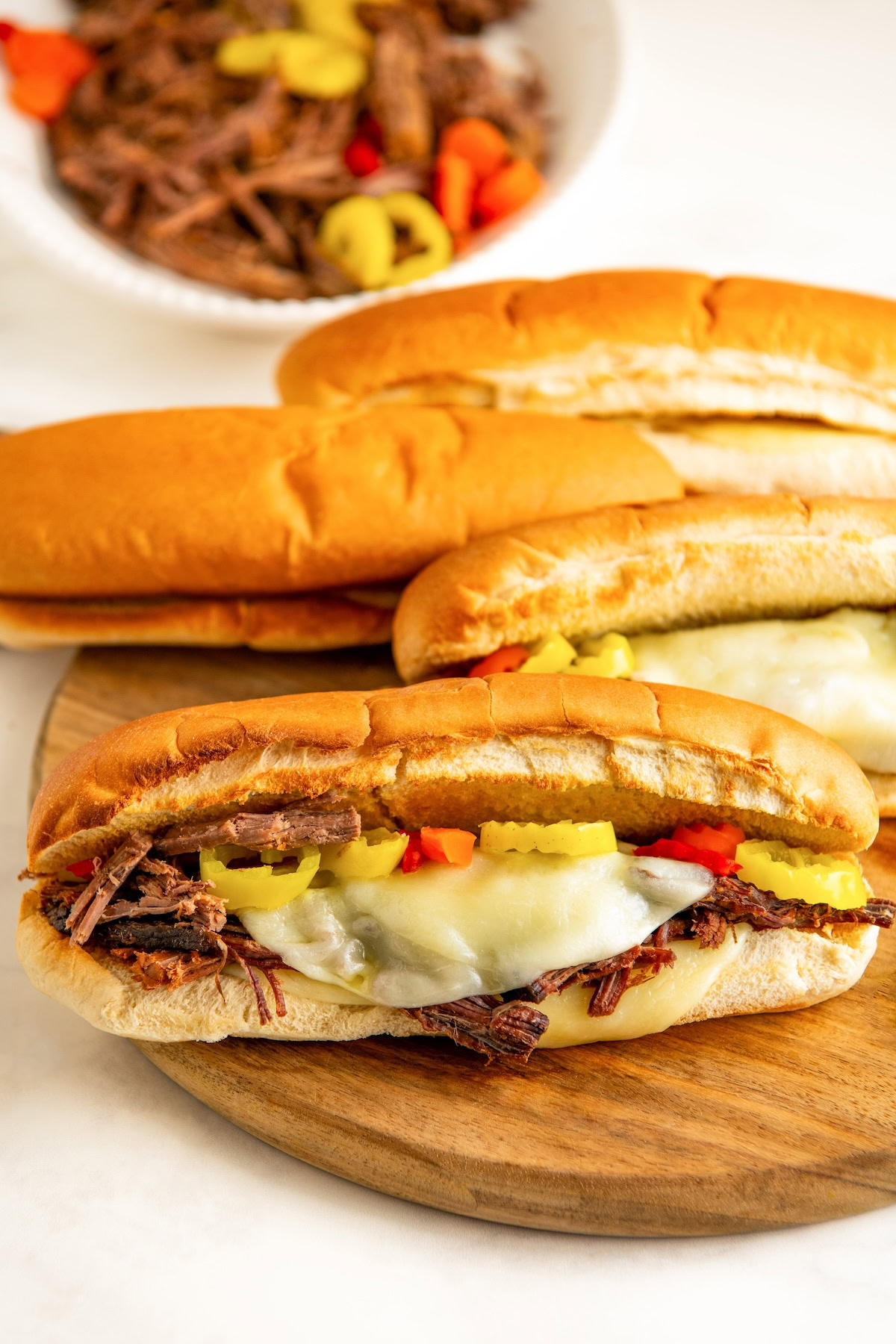 Several Italian beef sandwiches on freshly-toasted bread, with melty cheese and pickled veggies.