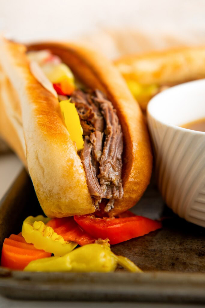 Close-up of slow cooker Italian beef sandwiches with crunchy pickled veggies and pepperoncinis after being dunked in the au jus.