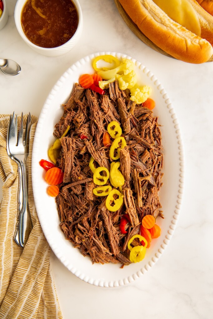 A plate of juicy shredded beef is topped with extra peppers. 