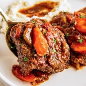 A serving spoon placing a tender crockpot Swiss steak on a plate.