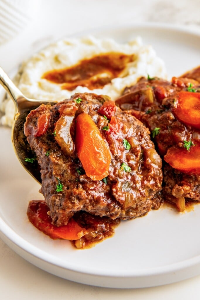 A serving spoon placing a tender crockpot Swiss steak on a plate.