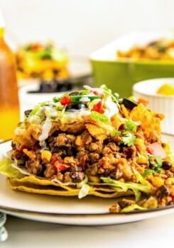 A serving of taco casserole with fritos on top of two crispy tortilla shells on a plate.
