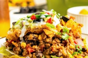 A serving of taco casserole with fritos on top of two crispy tortilla shells on a plate.
