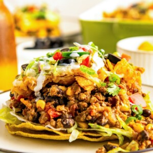 A serving of taco casserole with fritos on top of two crispy tortilla shells on a plate.