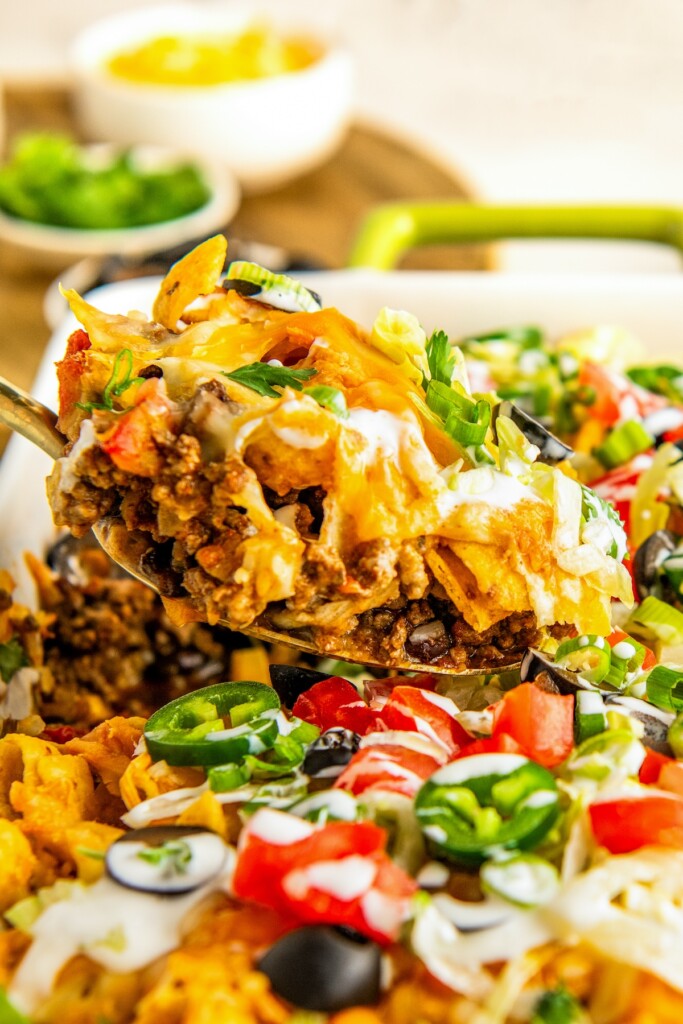 A large spoon scooping out a serving of taco casserole with fritos out of a casserole dish.