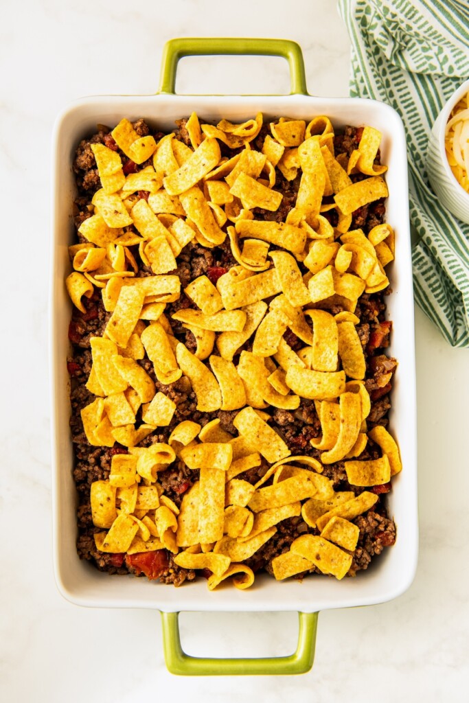 Ground beef and fritos being arranged in a casserole dish.