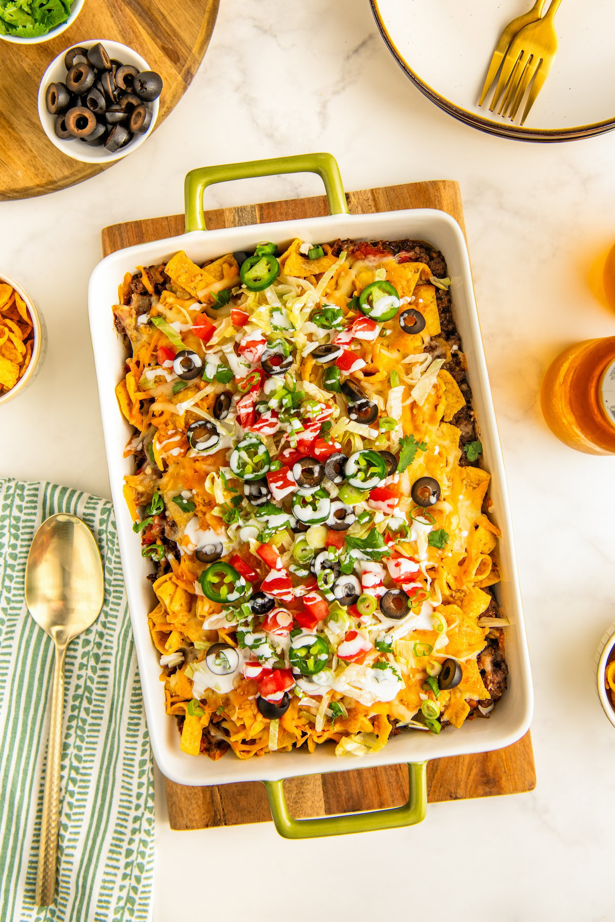 Freshly baked taco casserole set on a cutting board with all the garnishes arranged on top and drizzled with sour cream.