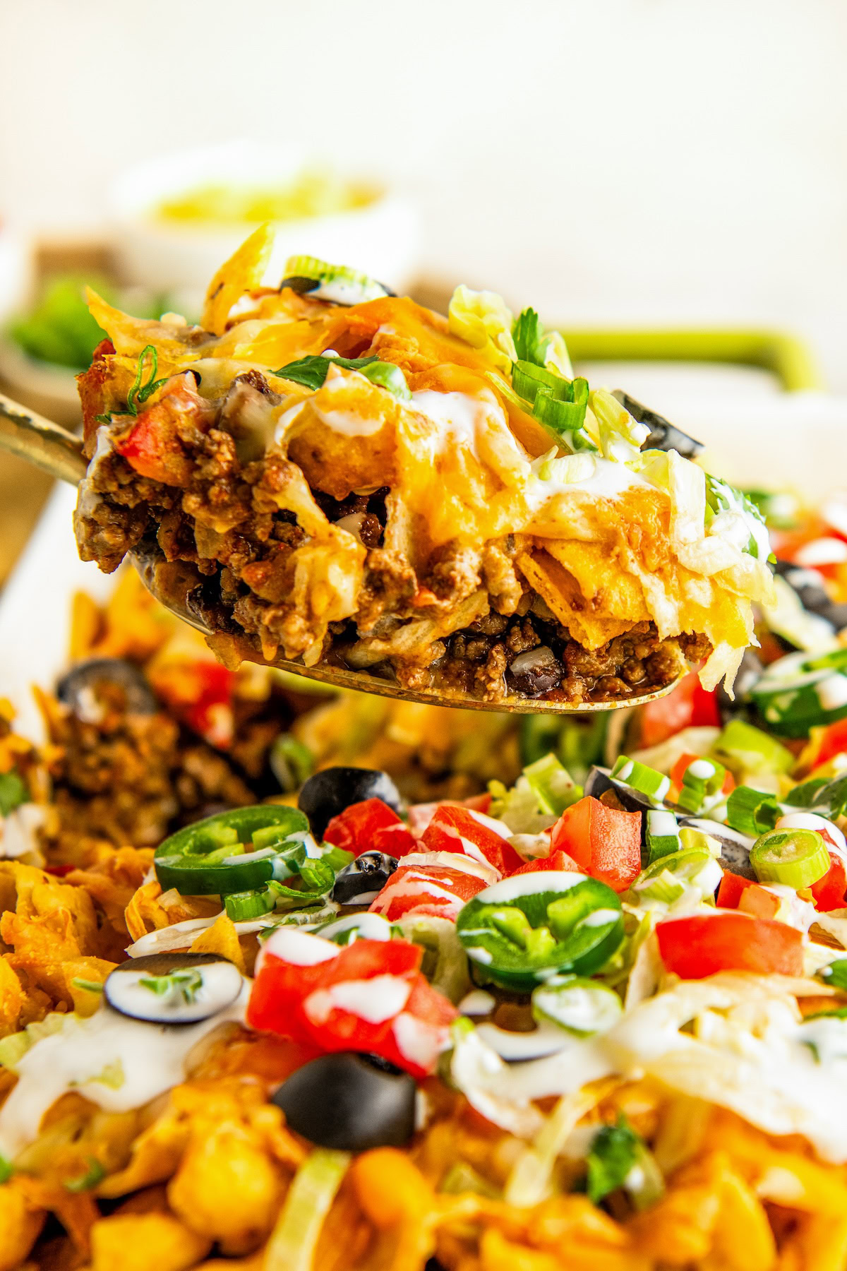 A large spoon scooping out a serving of beef taco casserole with fritos.