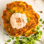 A golden, crispy corn fritter is garnished with micro greens.