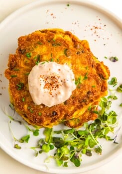 A golden, crispy corn fritter is garnished with micro greens.