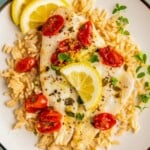 Plate of flaky fish with juicy tomatoes and lemon slices over fluffy rice.