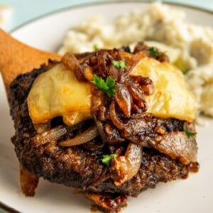 A single serving of french onion cube steak is being plated next to mashed potatoes.