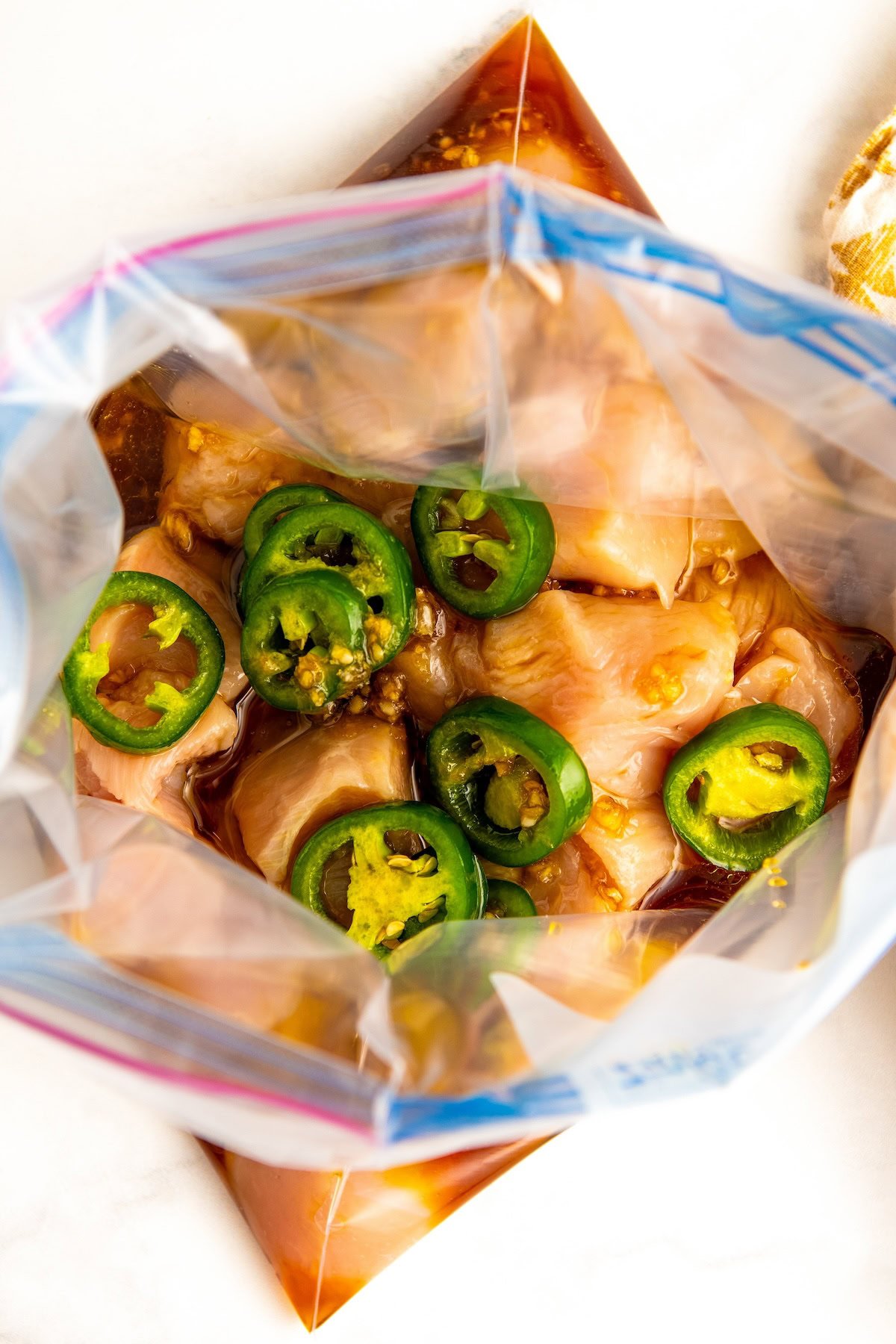 Chicken breasts are in a large zip-top gallon bag with grilled chicken marinade and sliced peppers. 