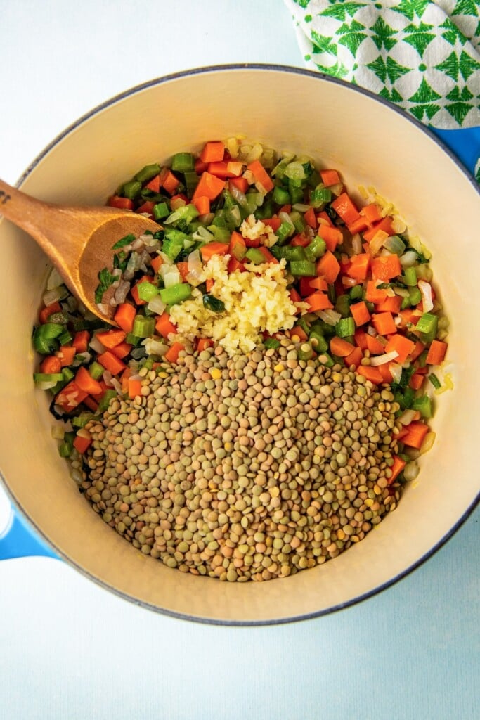 Adding the veggies, garlic, and dried lentils to the pot.