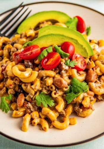 A plate of Mexican mac and cheese with tomatoes, sliced avocado, and fresh cilantro.