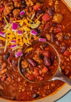 A large pot of ground turkey chili with three kinds of beans with a ladle scooping out a serving.