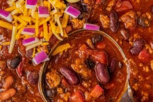 A large pot of ground turkey chili with three kinds of beans with a ladle scooping out a serving.