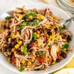 A large serving bowl of juicy slow cooker Mexican chicken with rotel with a large spoon on the side and fresh cilantro sprinkled on top.